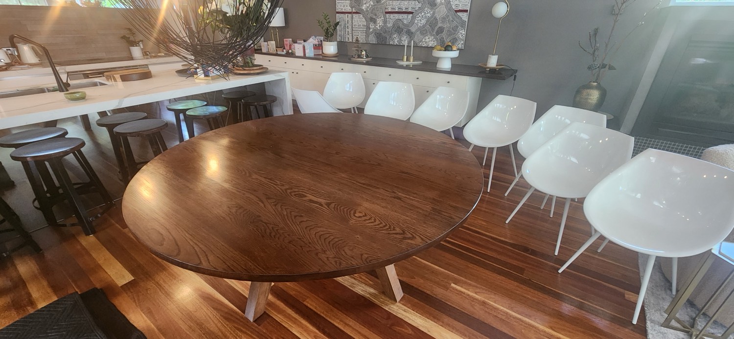 The same round oak dining table after restoration, refinished in water-based polyurethane showing the grain